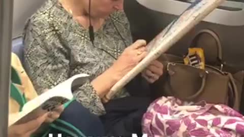 Woman cross stitching on subway train holds frame with a string tied to her ear
