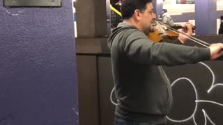 Guy plays violin together with another guy playing cello across subway station