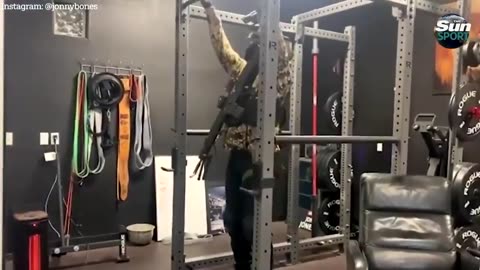 Jon Jones doing pull ups in a spec ops outfit with a Rifle