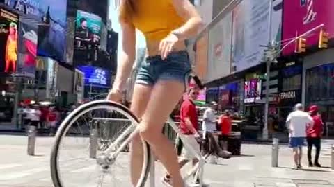 A beautiful woman rides a bicycle with one hand