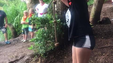 Girl in black shorts black shirt red bandana rope swings into water