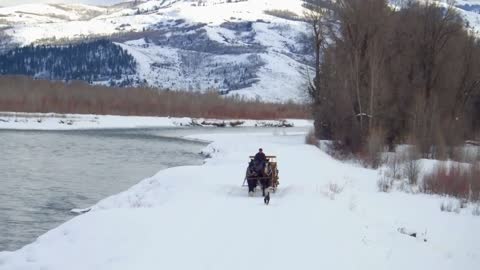 Horse and carriage travel alongside river and snow covered mountains