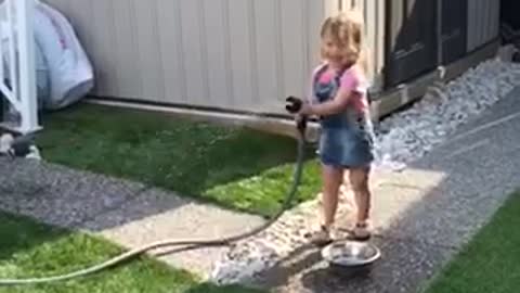 Little girl entertains French Bulldog with water hose