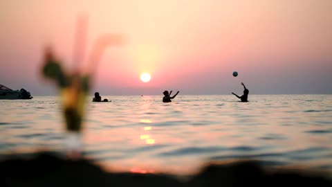People playing ball in the ocean at sunset