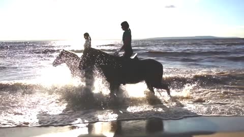 Two women ride on horse at river beach in water sunset light