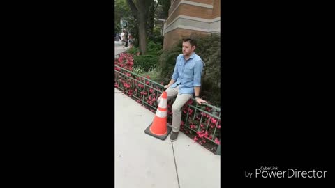 Guy in blue button up and khakis crosses the street and back with orange traffic cone