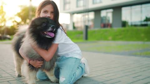 Brunette girl hugs a fluffy dog at sunset outdoors