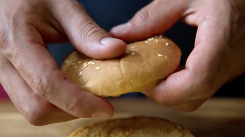 Close up of a Person Breaking a Hamburger Bun in Half