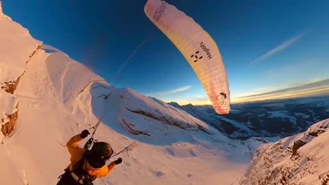 Paraglider Flies and Skis Over Golden Hour Mountains