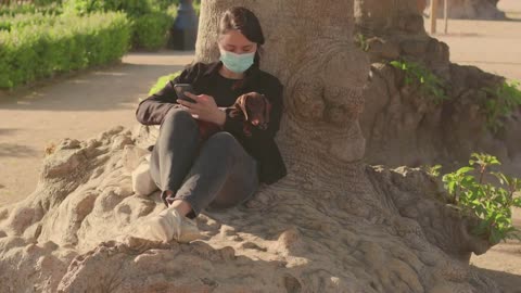 Brunette caucasian girl in the mask in the park with her dog