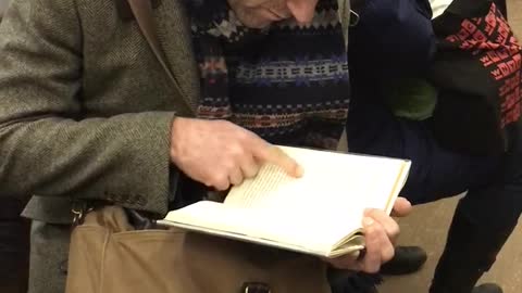 Old guy black beanie reading book pointing at words