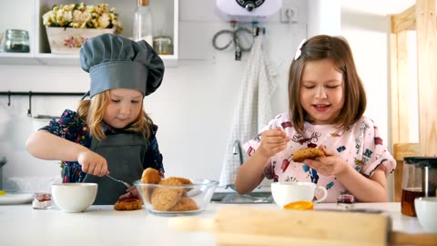 Two girls cute girl in the kitchen eating cookies with jam