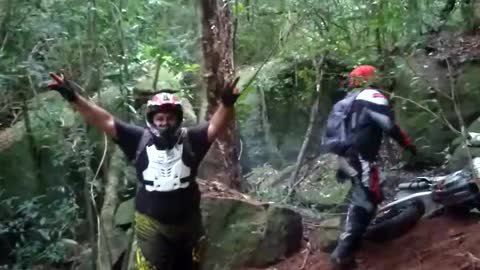 Biker drives up steep forest hill, bike flips back and falls