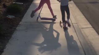 Two sisters racing on scooters, sister in front falls and trips other sister