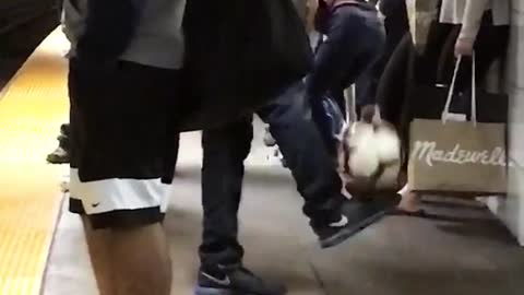 Guy black umbrella subway train station kicking balancing white soccer ball holding green soccer ball