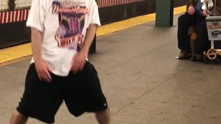 Man in white shirt dances to music from violin in subway station