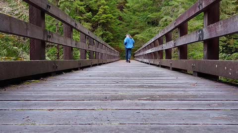 Man Running Away on a Wood Very High Trail Bridge Over a Rushing River.