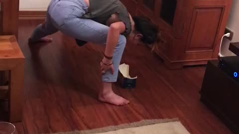 Green top girl on wood floor tries to pick up paper with mouth and faceplants