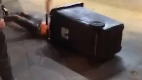 Man in beenie runs and dives head first into black garbage can