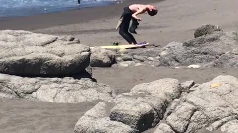 Guy in black suit bending back at beach