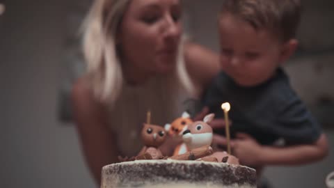 A Mother Helping His Son Blows Off The Candle Flame On His Birthday Cake