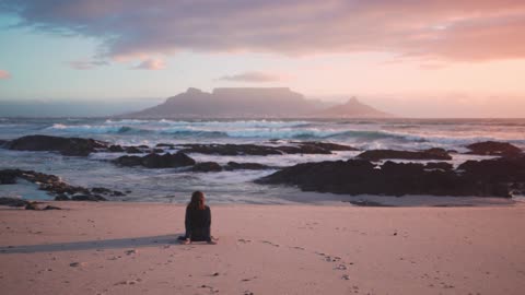 a woman seated on the beach sand enjoying the table mountain view