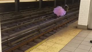 Woman in pink dress dances down subway train tracks