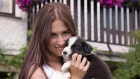 A young beautiful woman talks to, cuddles and kisses a cute little puppy