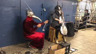 Two people in silver masks playing instruments