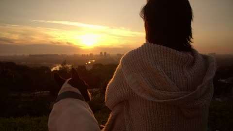 A woman with her dog watching the sunset