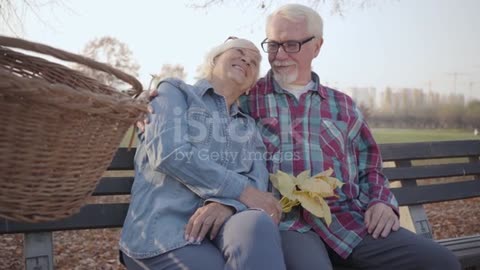 Side view of Caucasian retired man and woman sitting on the bench in sunlight and talking