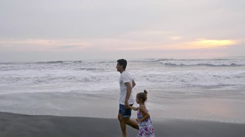 A Father Running With His Daughter On The Beach Sand