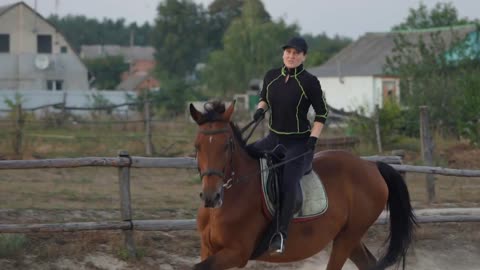 Horsewoman riding on brown horse and jumping the fence in sandy parkour riding arena