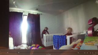 Blonde baby in red climbs out of white crib camera