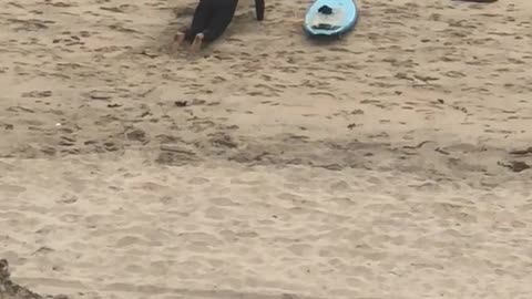 Guy in black wet suit practices blue surfboard