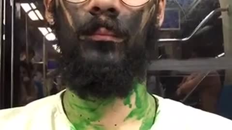 Guy with black and green painted face sits on subway