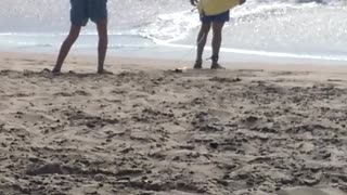 Guy in blue swim trunks takes picture for friends on beach holding yellow surfboard