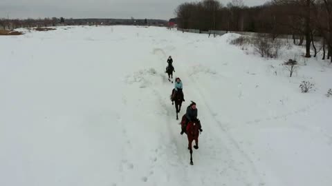 A group of young women riding horses on a snowy field. Going towards the camera