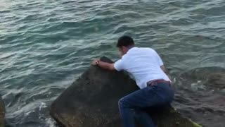 Guy tries to jump on some rocks beach almost slips into water