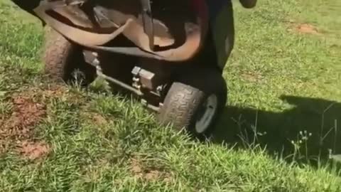 Kid drives red lawnmower up hill and it topples on top of him