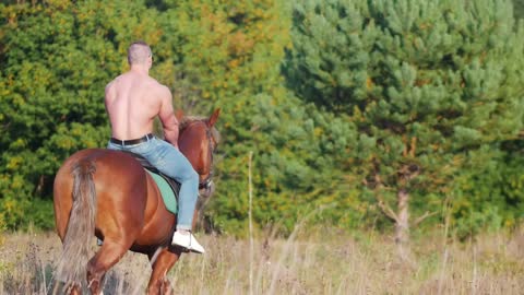 Man weightlifter on horseback moving towards the forest on the field