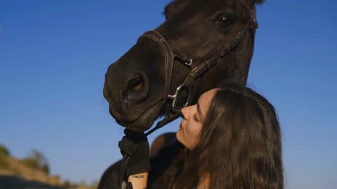 Side view of gorgeous young woman hugging purebred horse with clear blue sky at background