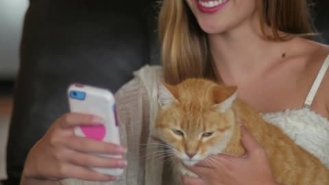 A young beautiful woman takes a selfie with an orange domestic shorthaired tabby cat