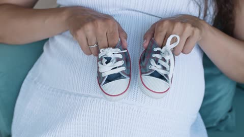Pregnant woman holding small baby shoes, top shot