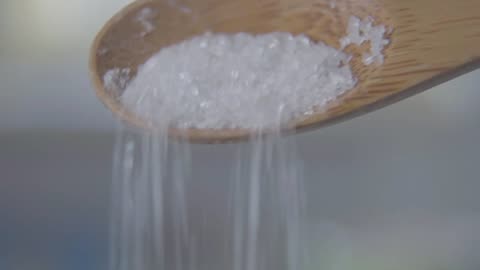 Closeup of sugar spilling from wooden spoon