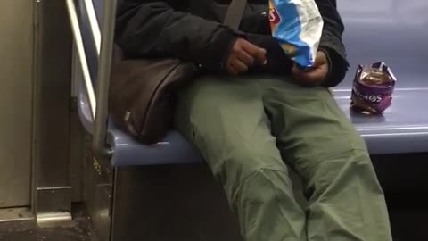 Guy is sleeping and also eats bags of doritos and lays chips on subway train
