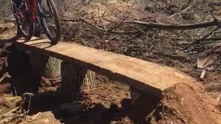 Guy red shirt white shorts tries to ride bike over wood falls off falls into branches