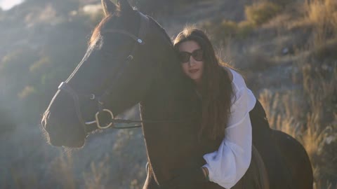 Brunette Caucasian woman in sunglasses hugging neck of brown horse