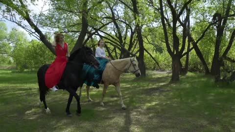 Two women are walking in the woods on horseback