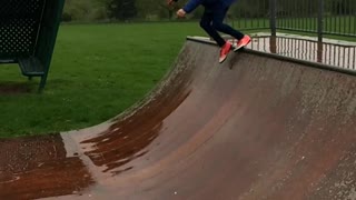 Blue jacket orange shoes girl slips on skateboard half pipe